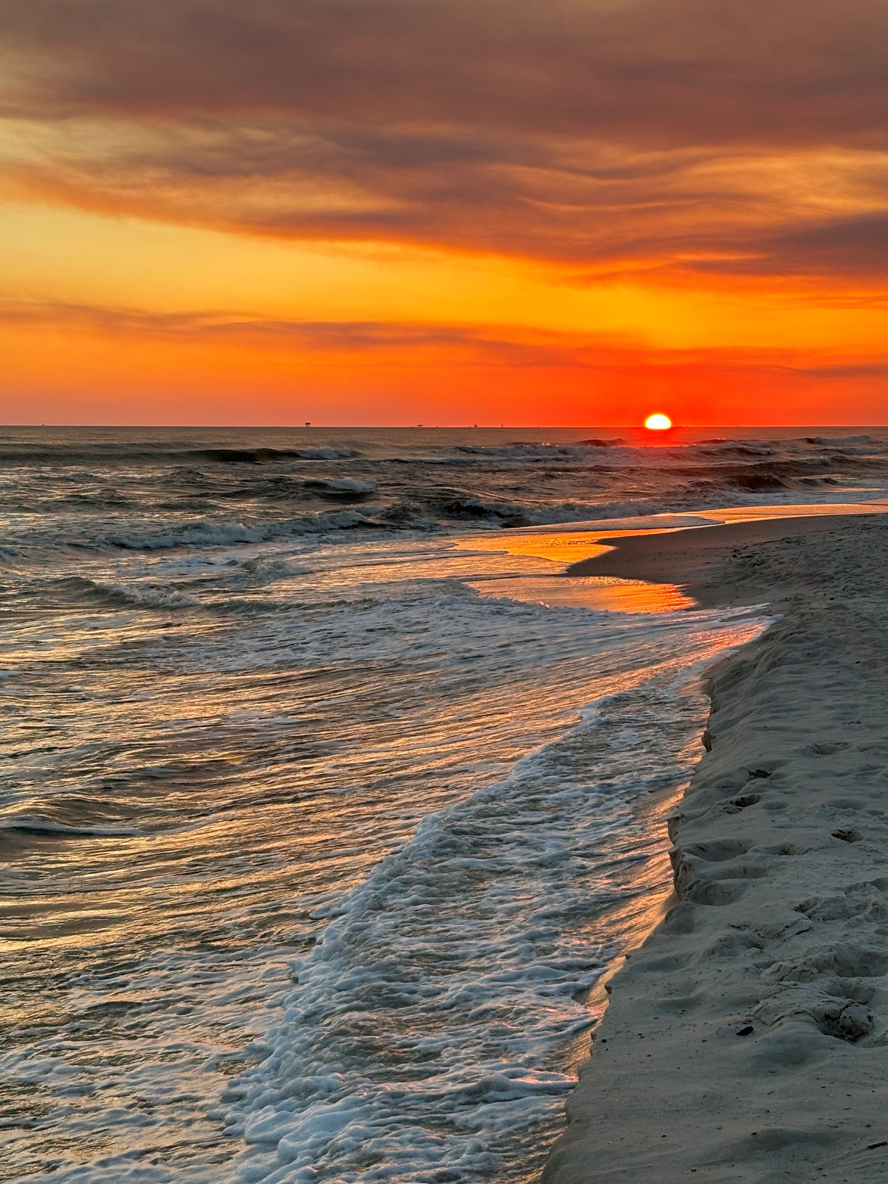 A sunset over a beach with waves gently lapping at the shore.