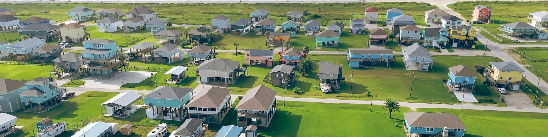 Panorama aerial view elevated colorful beach house in oceanside neighborhood with road access to sandy shoreline. Ideal vacation rental setup, car, UTV access, storm-safe in Port Bolivar, Texas