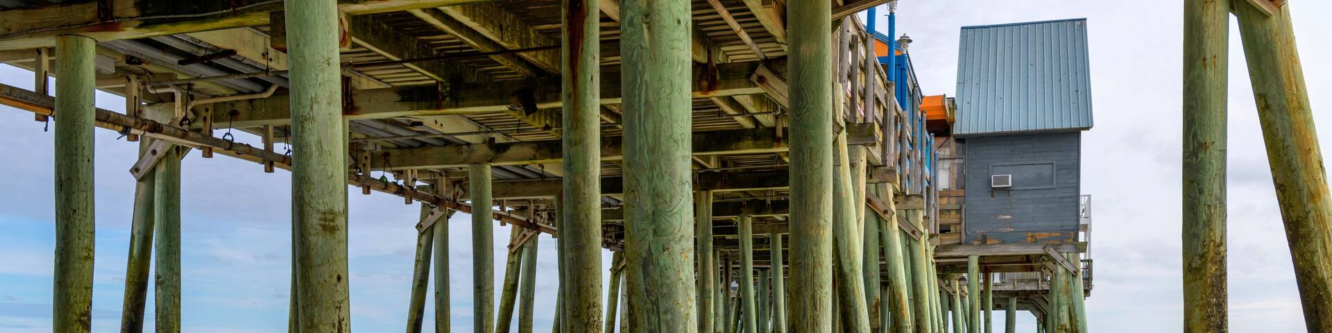 A pier with wooden supports extending into the water, a wooden structure on the pier, and a cloudy sky.