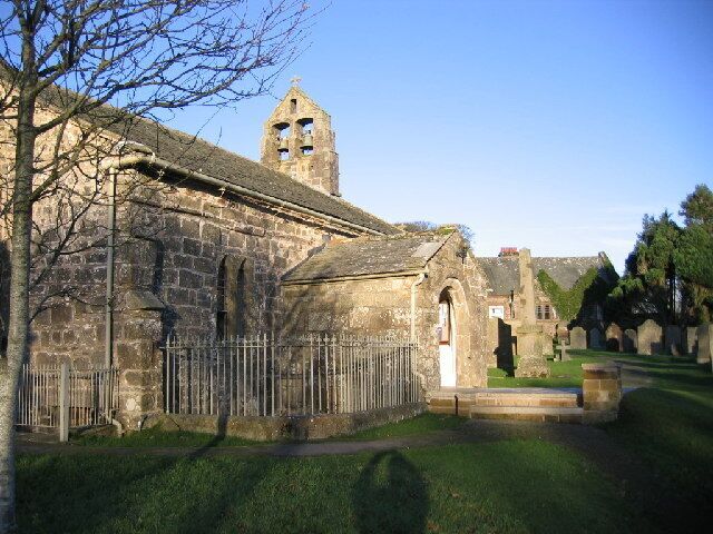 An old stone church with a bell tower and a cemetery in the background.