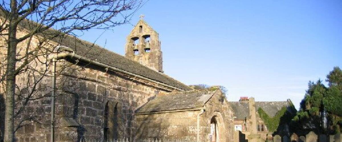 An old stone church with a bell tower and a cemetery in the background.