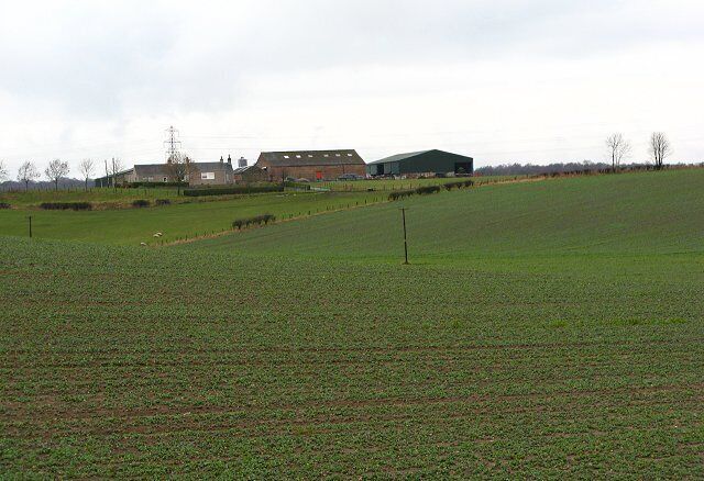 A green field with a barn and a house in the background.