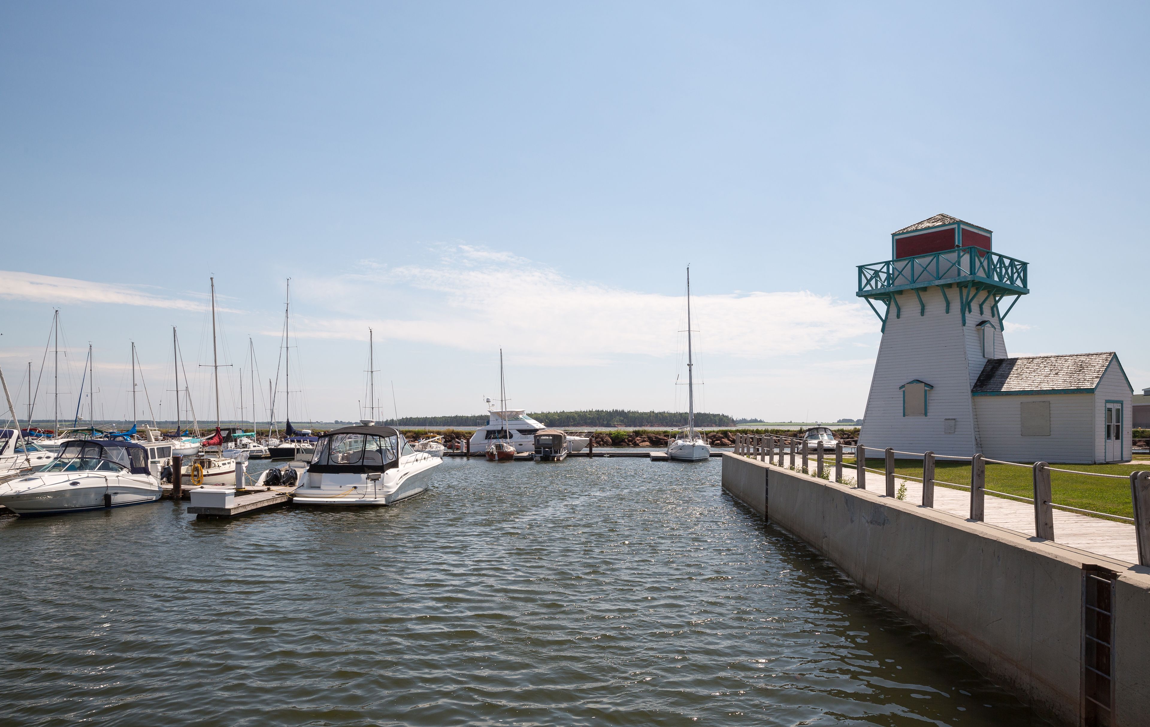 Un port de plaisance où sont amarrés plusieurs bateaux, un phare et une zone herbeuse avec un petit bâtiment.