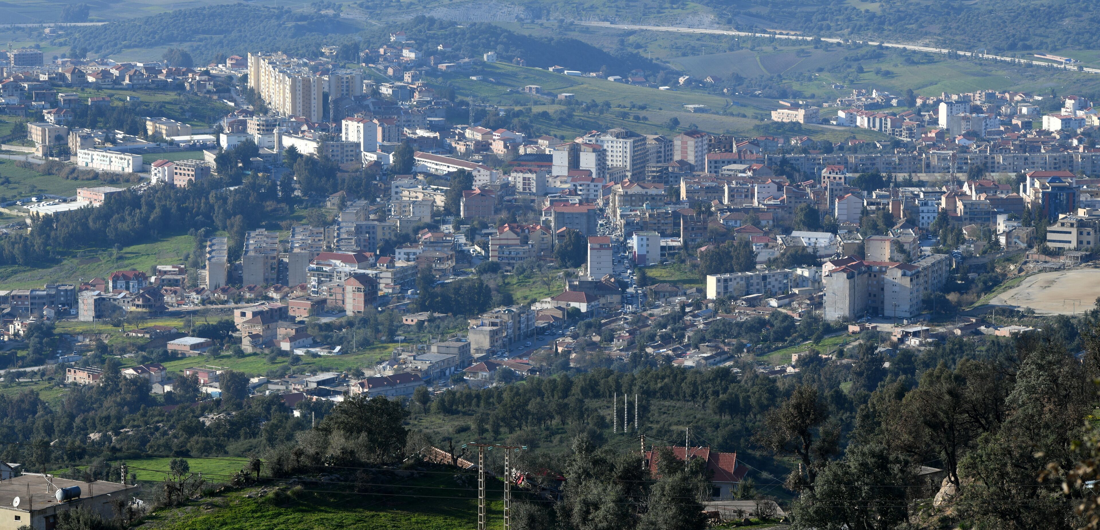 A densely populated urban area with a mix of residential and commercial buildings, surrounded by green hills and a coastline.