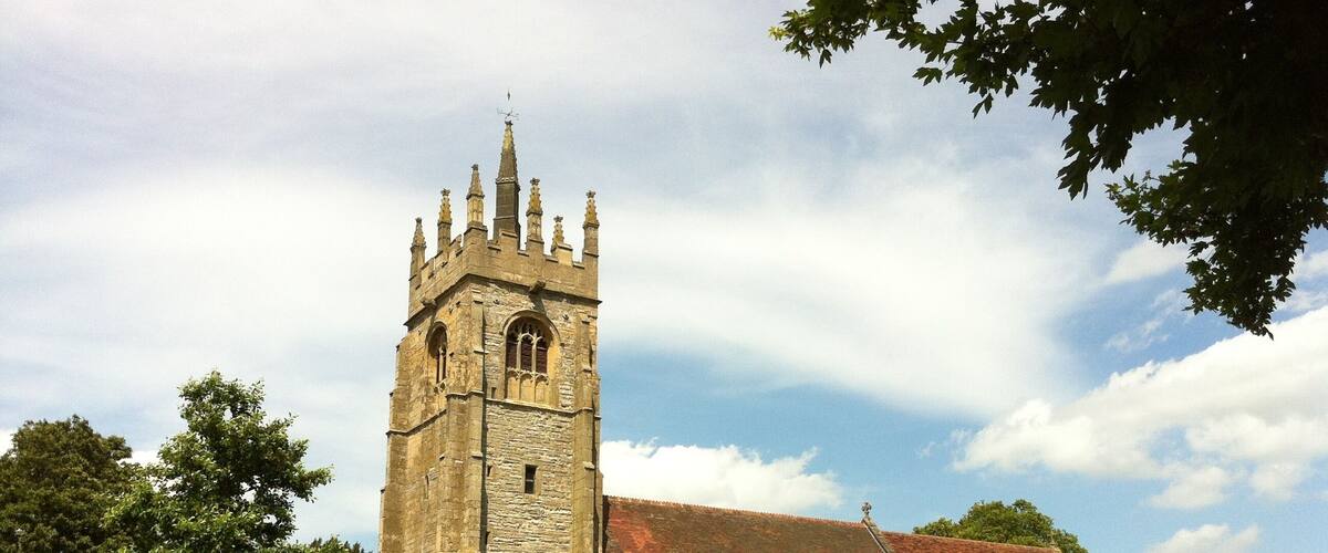 A church with a tall tower and a red-tiled roof, surrounded by a cemetery with numerous gravestones.