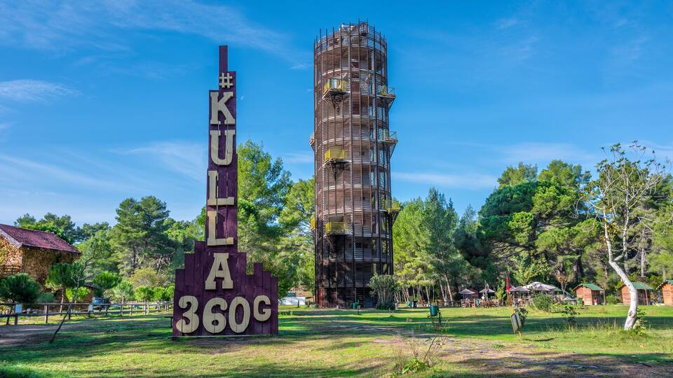 A tall, unfinished building with scaffolding, surrounded by trees and a sign reading "KULIA 360G".