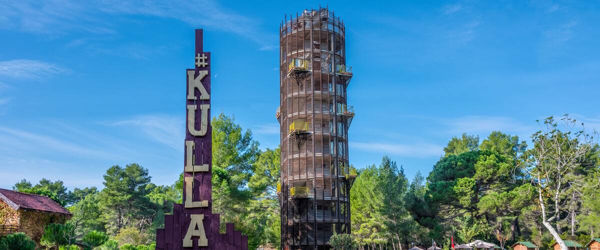 A tall, unfinished building with scaffolding, surrounded by trees and a sign reading "KULIA 360G".