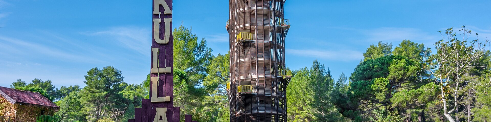 A tall, unfinished building with scaffolding, surrounded by trees and a sign reading "KULIA 360G".