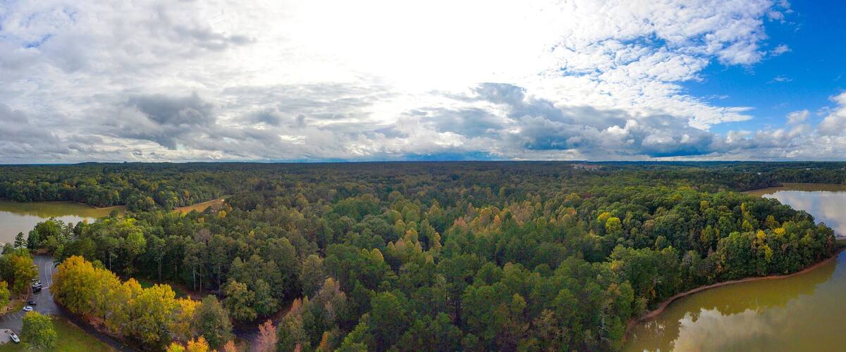 a breathtaking panoramic aerial shot of the still lake waters and vast miles of lush green and autumn colored trees with powerful cloud formations and blue sky at Sweetwater Creek State Park