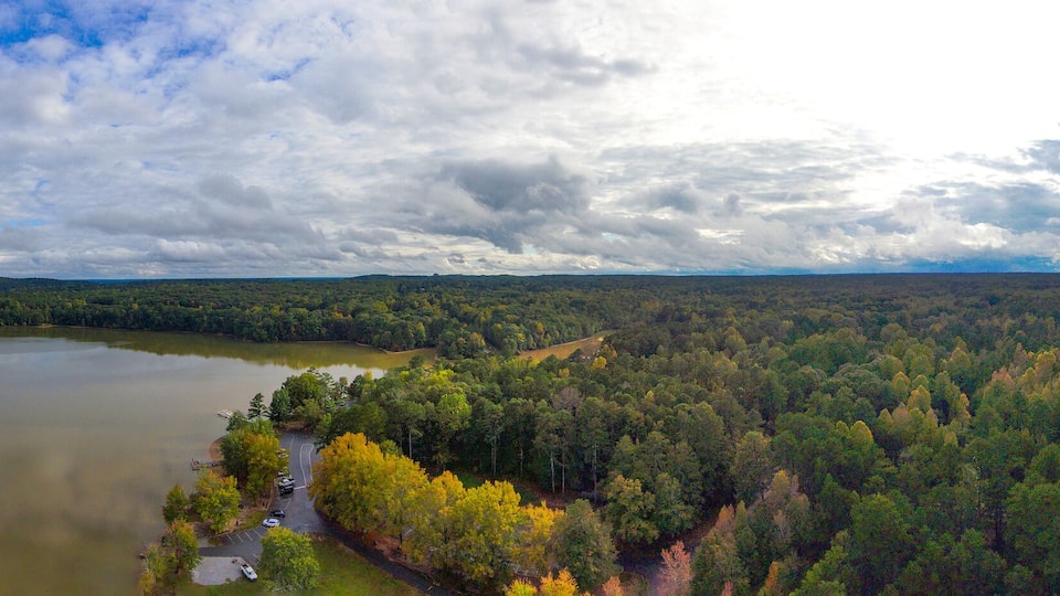 a breathtaking panoramic aerial shot of the still lake waters and vast miles of lush green and autumn colored trees with powerful cloud formations and blue sky at Sweetwater Creek State Park
