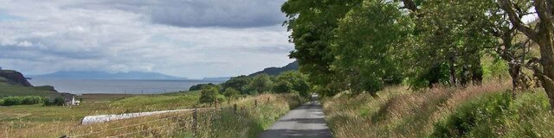 Approaching Orbost. This is the attractive tree-lined road into Orbost from Lonmore. The island of Rum is visible on the distant horizon.