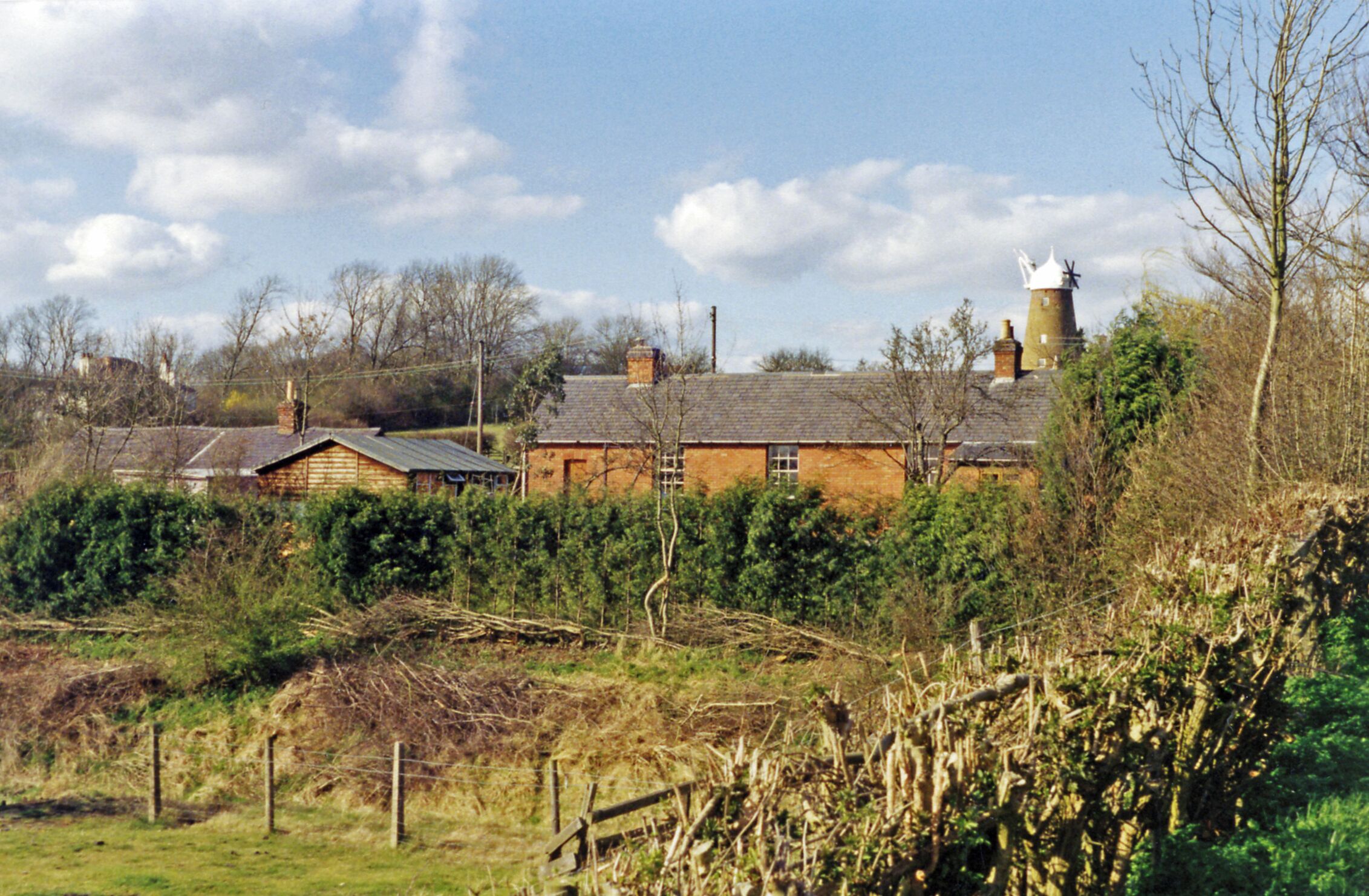 A rural landscape with a windmill, a brick house, and a field.