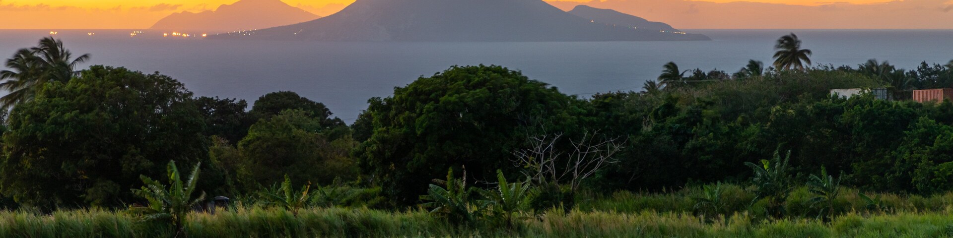 Un atardecer sobre un paisaje costero con una montaña destacada al fondo.