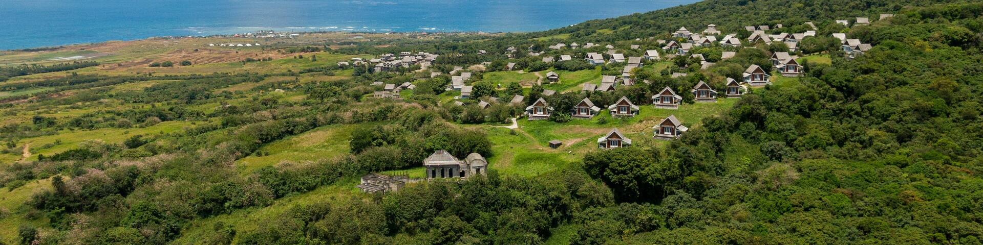 A coastal village with houses on a hillside, surrounded by lush greenery and the ocean.