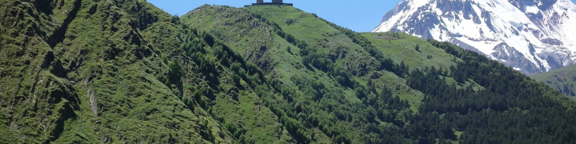 A mountain with a snow-capped peak and a small structure on a green hill.
