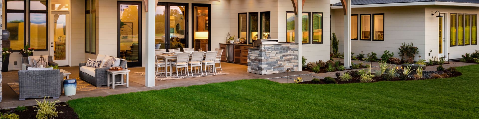 New luxury home exterior at sunset. Features large covered patio with barbecue, outdoor kitchen, and furniture
