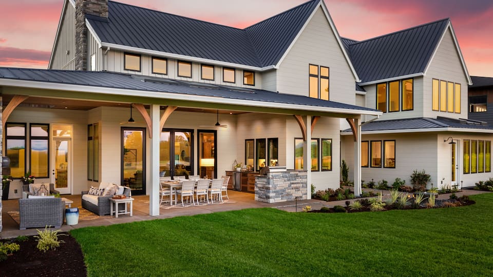 A modern two-story house with a covered patio, large windows, and a well-maintained lawn.