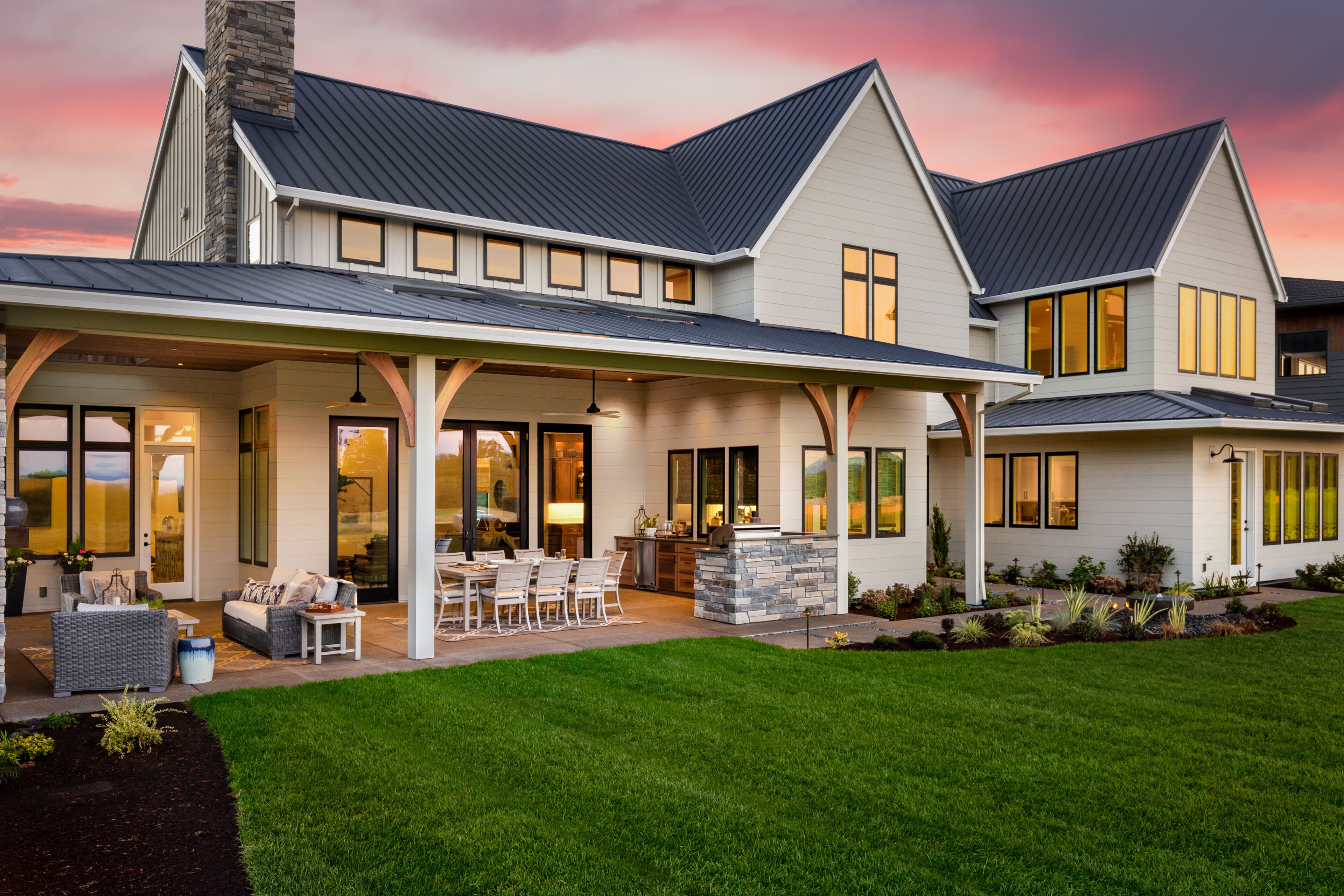 A modern two-story house with a covered patio, large windows, and a well-maintained lawn.