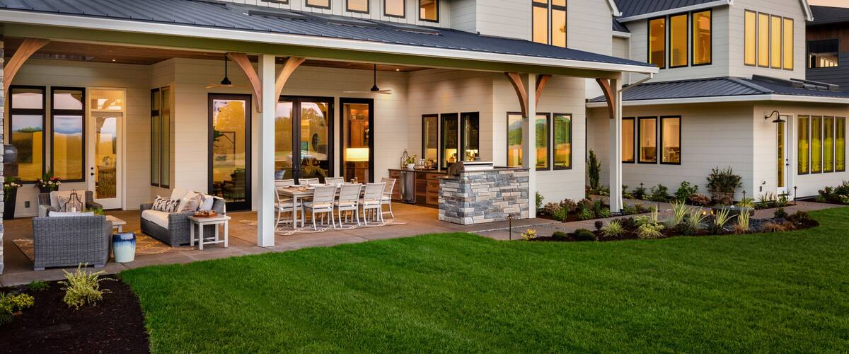 A modern two-story house with a covered patio, large windows, and a well-maintained lawn.