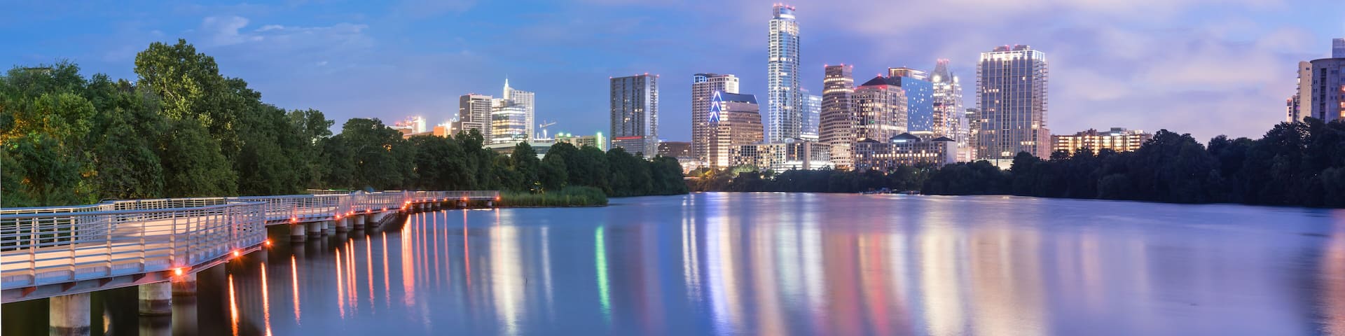 Panorama view of Downtown Austin, Texas, USA skylines reflection on the Colorado River at twilight. View from Ann and Roy Butler Hike-and-Bike Trail and boardwalk at Lady Bird Lake is on the left.