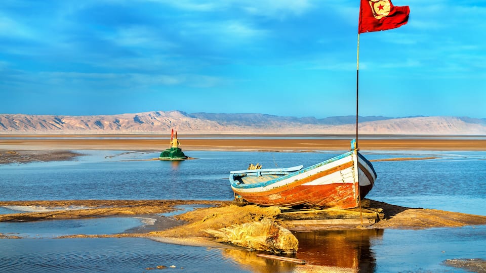 A boat with a flag on a rocky shore with a desert landscape in the background.
