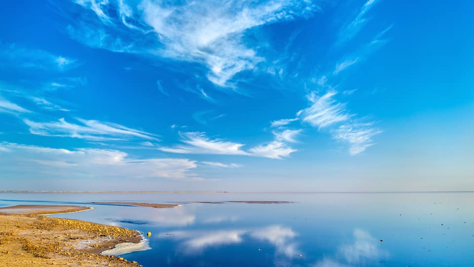 A calm lake with a clear blue sky and scattered clouds.