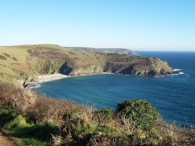 A coastal landscape with a beach, cliffs, and a clear blue sky.