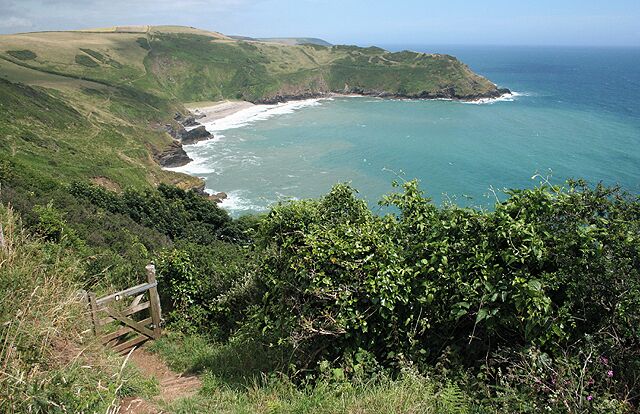 A coastal landscape with a grassy hillside, a wooden fence, and a view of the ocean.