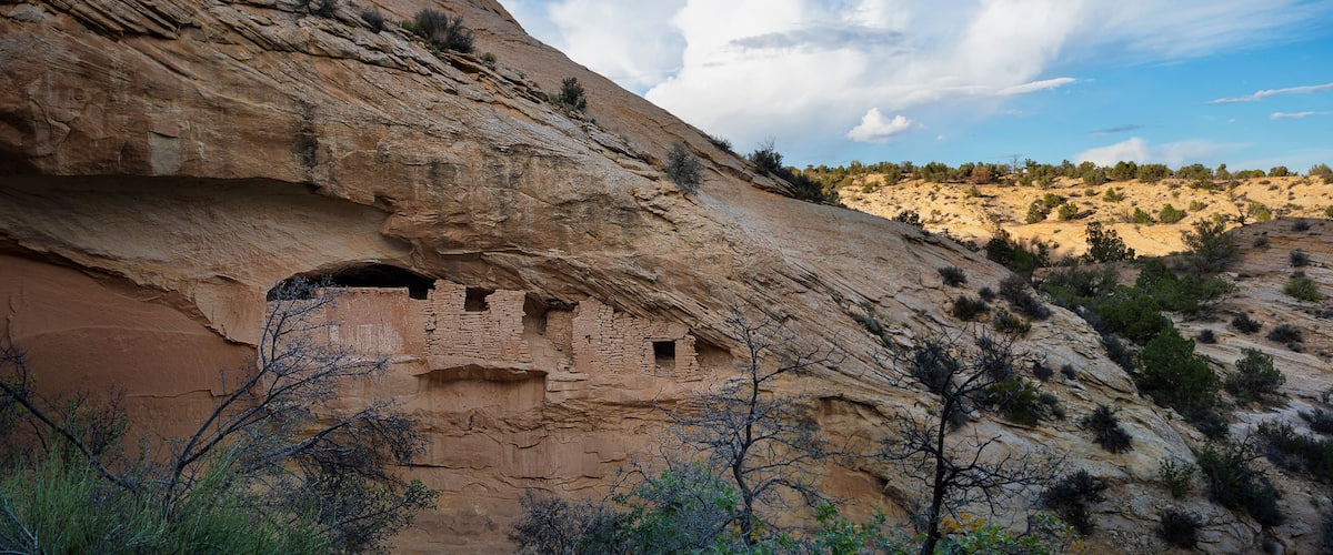 A rock formation with ancient cliff dwellings and sparse vegetation.
