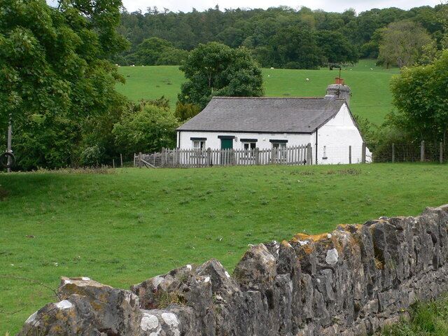 Una casa blanca con techo gris, rodeada por un muro de piedra y un campo verde.