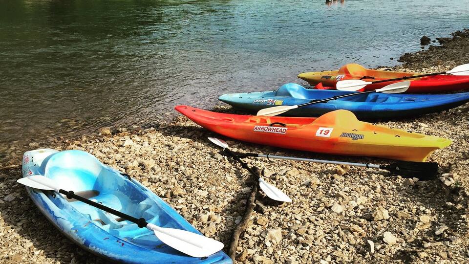 Kayaks on a rocky shore by a calm river with trees in the background.