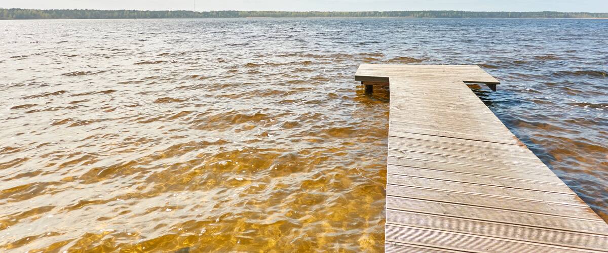 A wooden pier extending into a lake with clear water and a distant tree line under a partly cloudy sky.