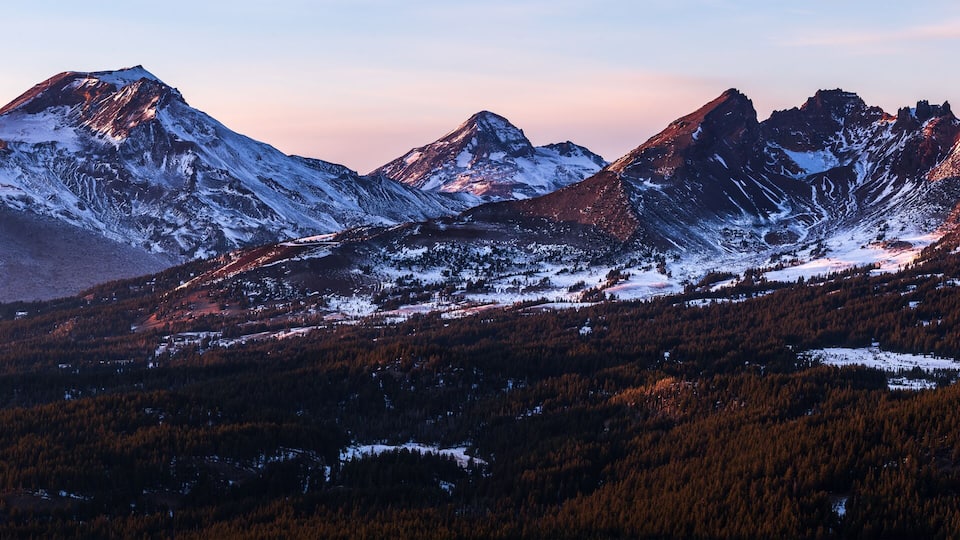 A snow-covered mountain range with prominent peaks and dense forested valleys.