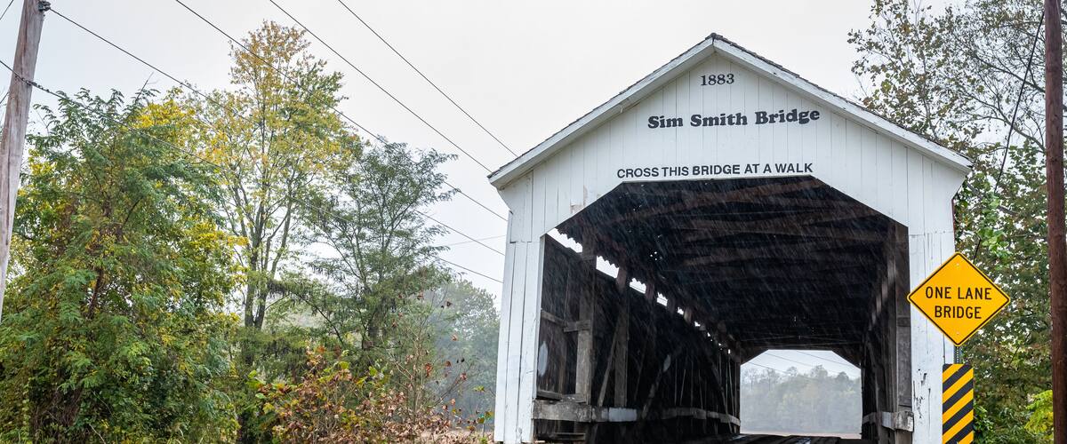A covered bridge named Sim Smith Bridge with a sign indicating it is a one-lane bridge.