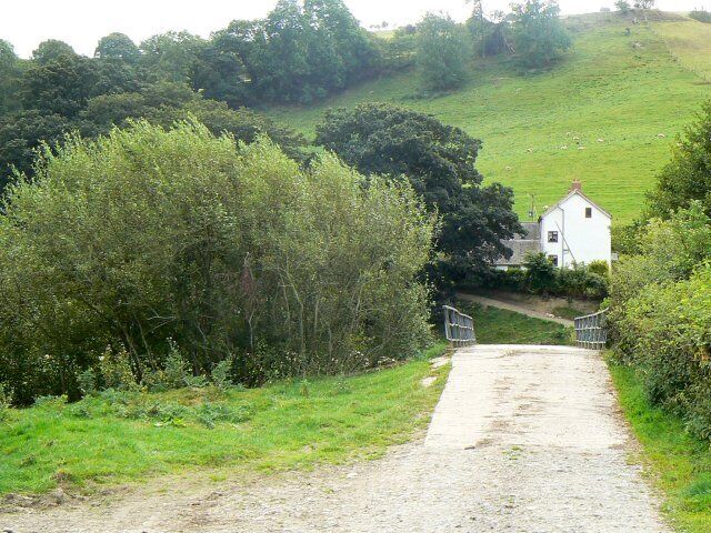 A rural path leading to a white house surrounded by greenery and trees.