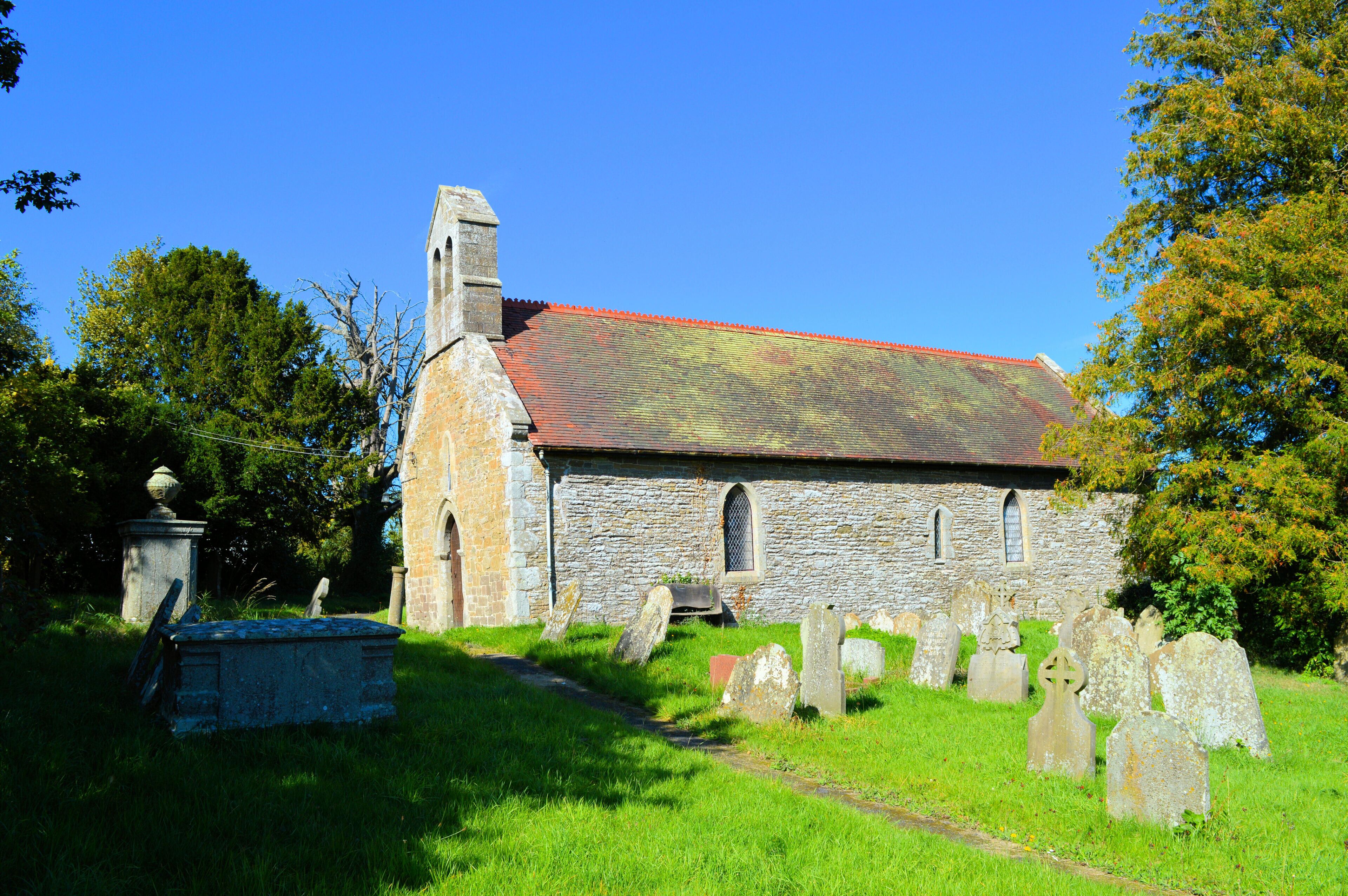 A stone church with a red roof, surrounded by a graveyard with headstones.
