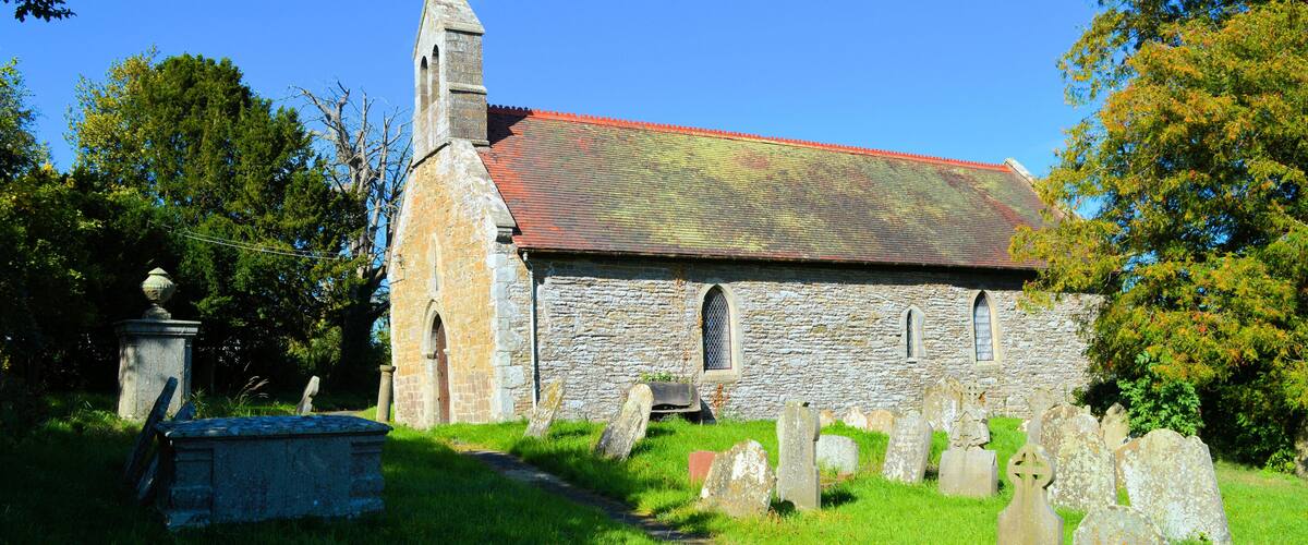 A stone church with a red roof, surrounded by a graveyard with headstones.