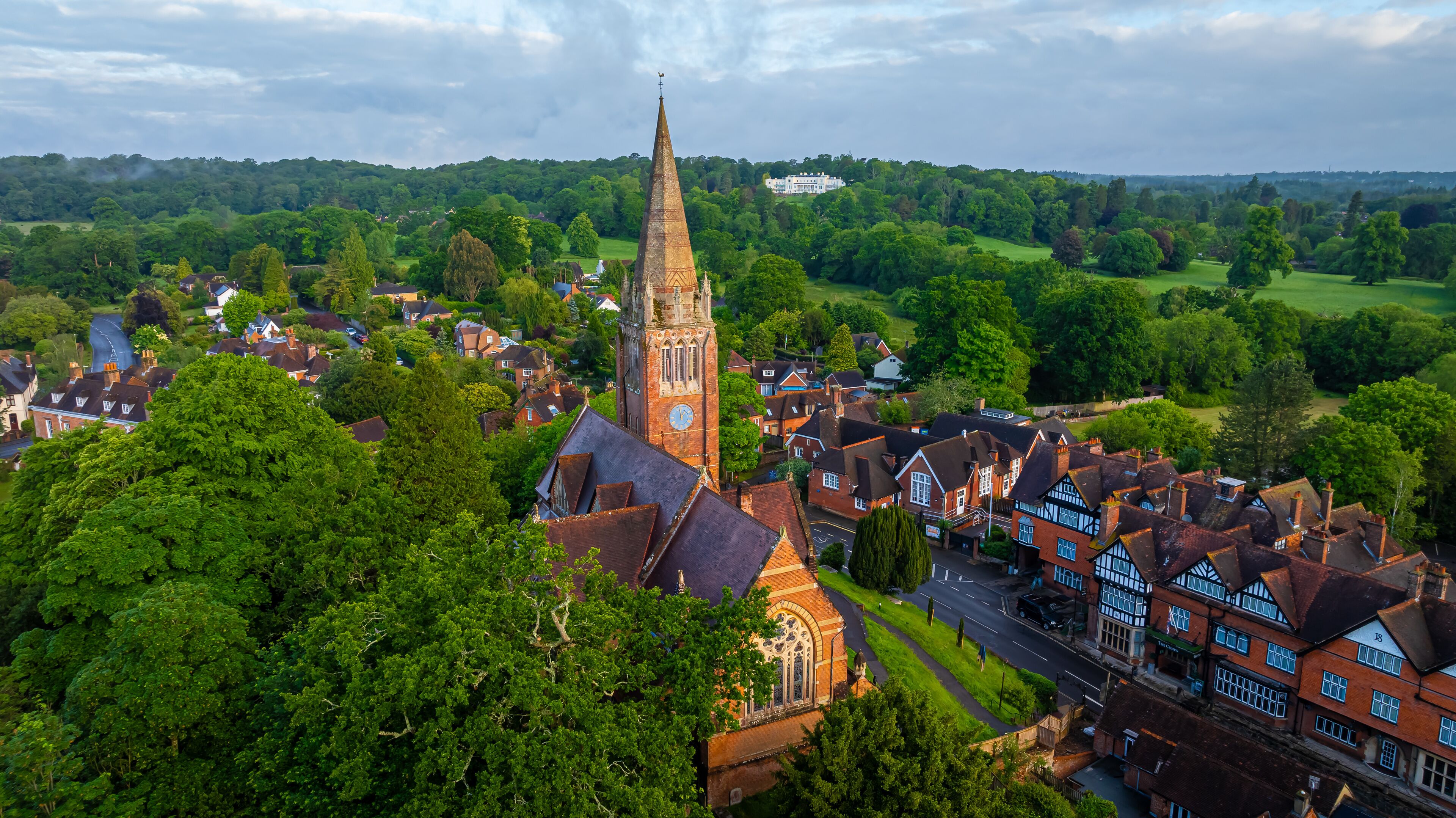 A historic town with a prominent church tower, lush greenery, and a large estate in the background.