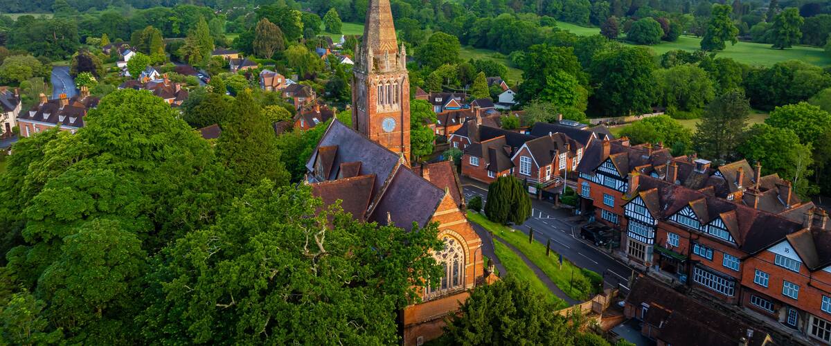 A historic town with a prominent church tower, lush greenery, and a large estate in the background.