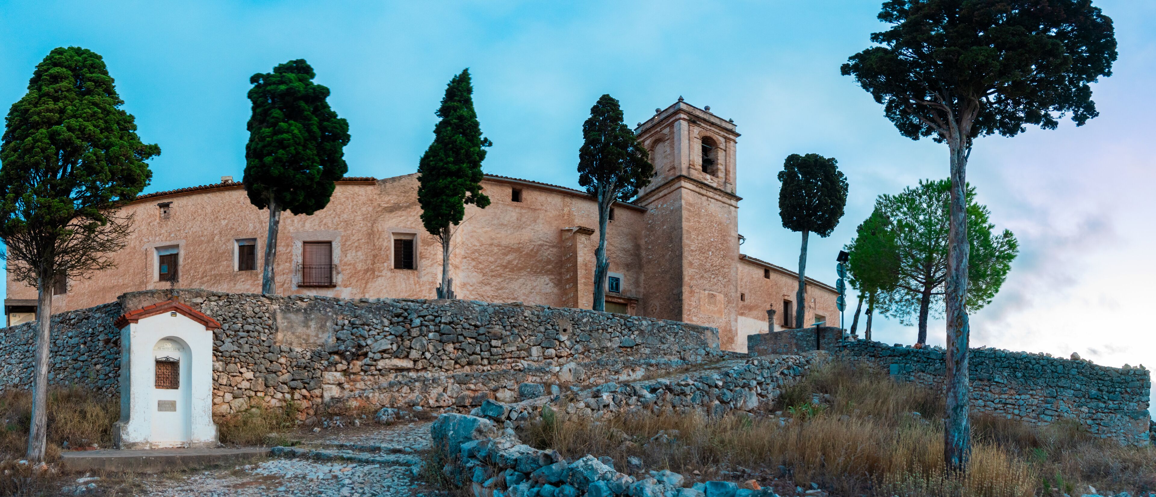 A stone building with a bell tower, surrounded by trees and a stone wall.