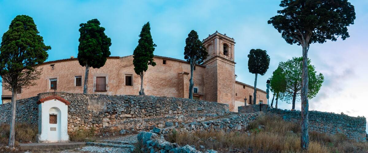 A stone building with a bell tower, surrounded by trees and a stone wall.