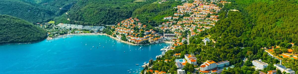 Panoramic aerial view of a coastal town of Rabac with red-roofed buildings nestled between lush green hills and turquoise waters of the Adriatic Sea. Croatia