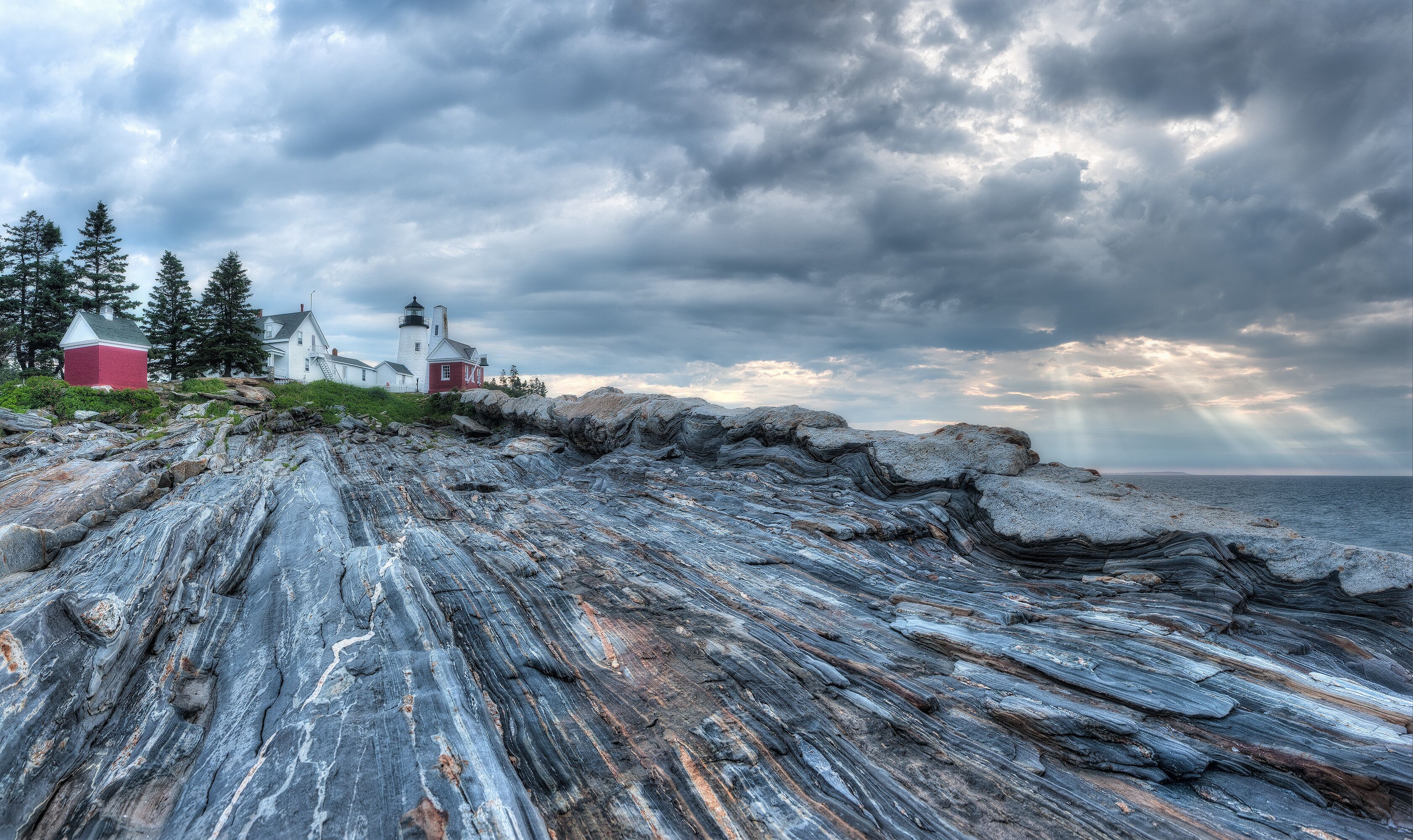 A rocky shoreline with a lighthouse and red buildings.