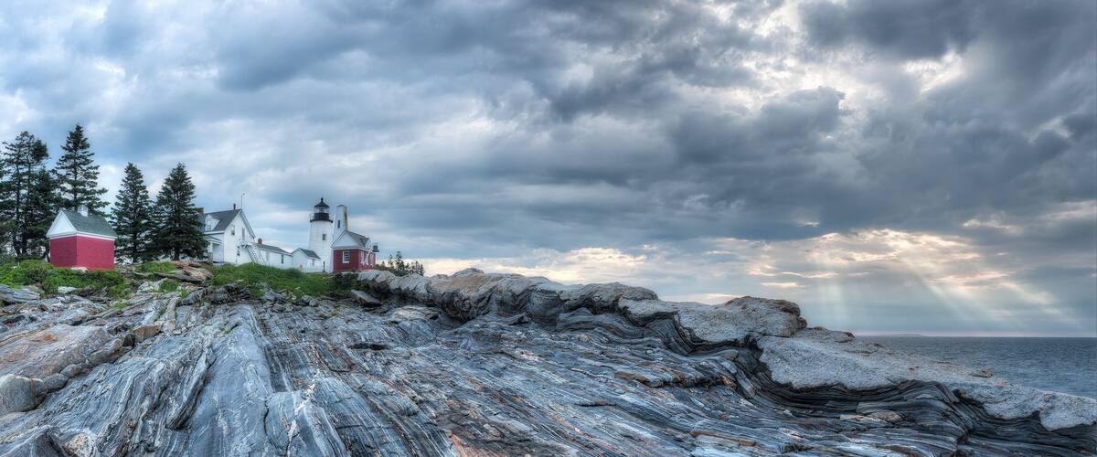 A rocky shoreline with a lighthouse and red buildings.