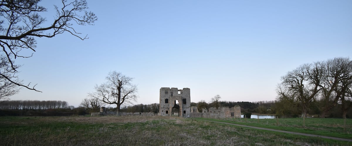 A historical stone structure in a grassy field with trees around.