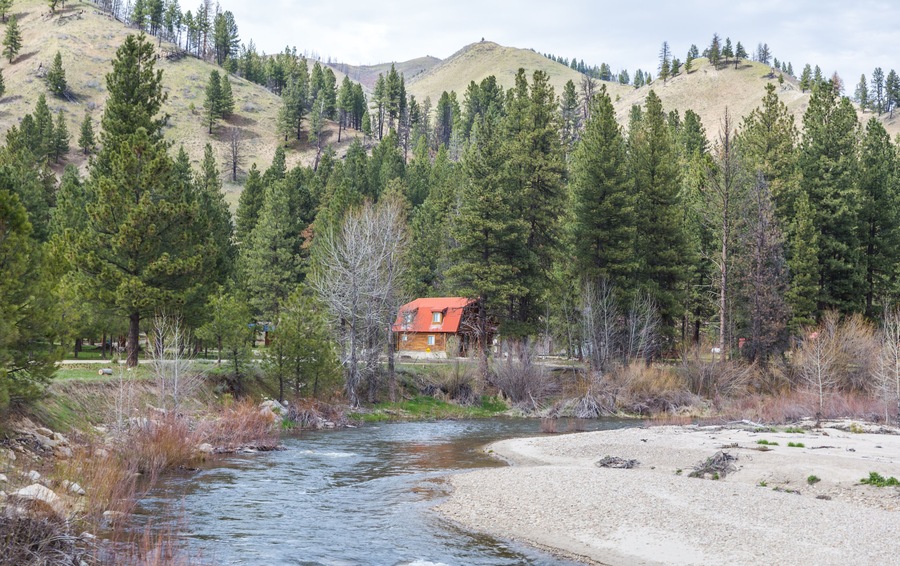 Cabin with Red Roof on River in Forested Area