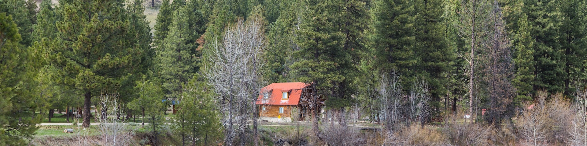 Cabin with Red Roof on River in Forested Area