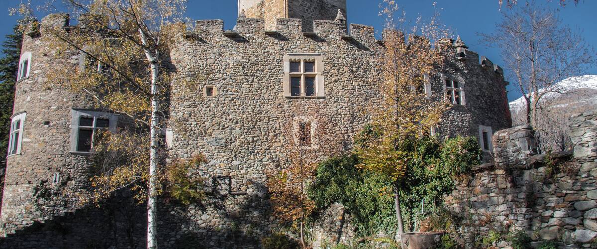 A stone castle with a bell tower, surrounded by trees and a grassy area.