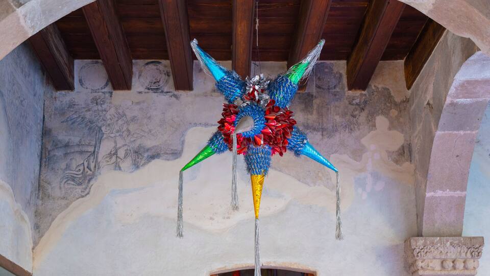 A colorful, intricately designed hanging ornament in a historical building with stone arches and a wooden ceiling.