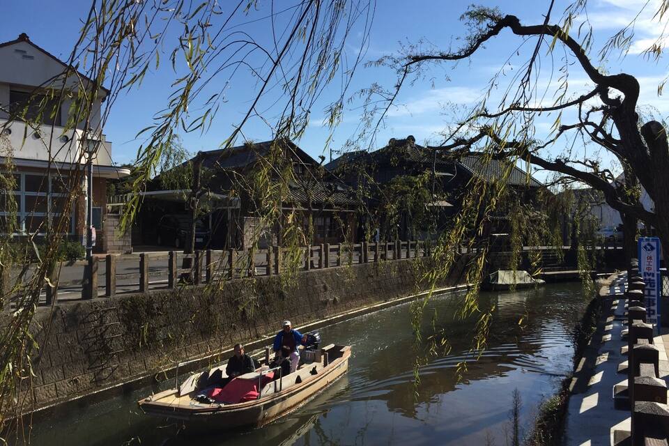 En traditionell träbåt på en kanal, med byggnader och träd i bakgrunden.